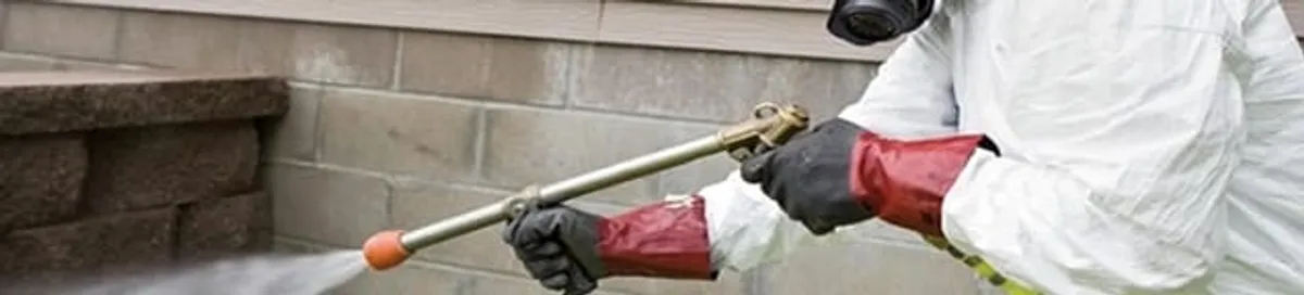 Pest control technician applying exterior insect treatment along a home foundation in Boise, ID