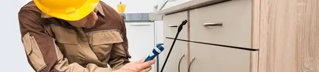 Roach exterminator applying treatment under kitchen cabinets in Boise, ID