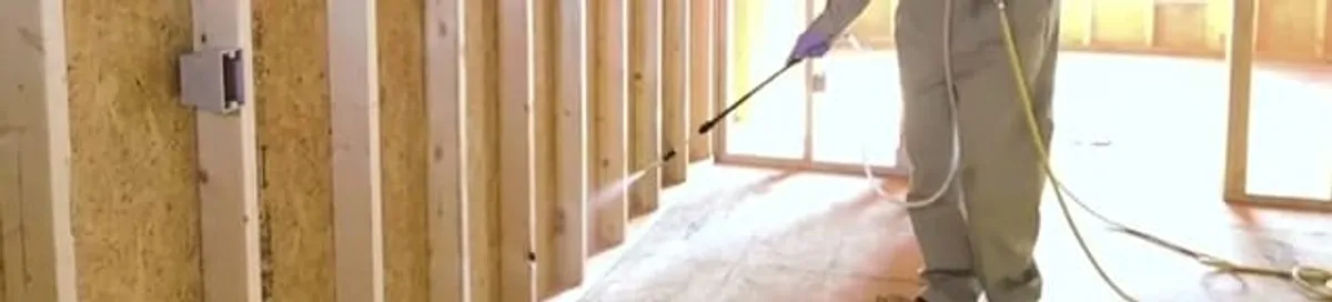 Termite treatment technician applying spray along framing and unfinished walls in Boise, ID